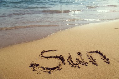 Kelime güneş el yazısıyla kumsalda, su hattının yanında.