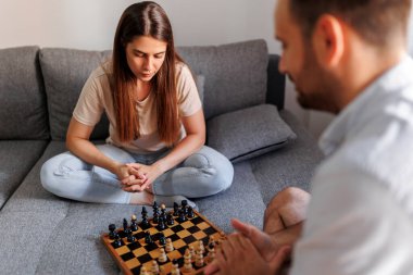 Aşık bir çift oturma odasında kanepede oturup satranç oynayarak ve evde vakit geçirerek eğleniyor.