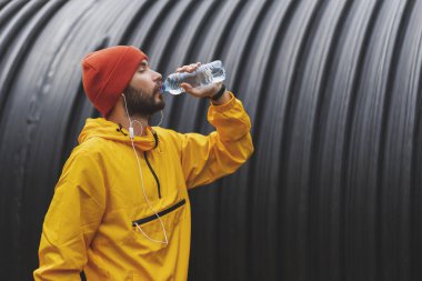 Atletik bir adam bulutlu bir kış gününde dışarıda koşuya ara verirken su içiyor.