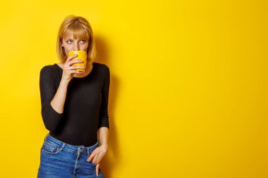 Sarı arka planda izole edilmiş ve fotokopi alanı olan kahve içen güzel genç bir kadın.
