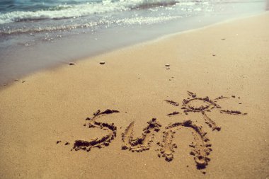 Kelime güneş el yazısıyla kumsalda, su hattının yanında.