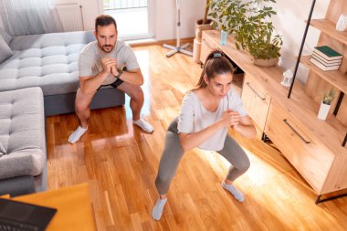 Çift evde çalışırken çömelirken yüksek açılı görünüm; çift online ev antrenmanı yapıyor 