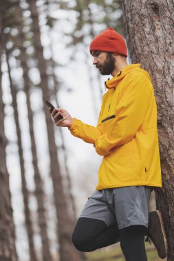 Bulutlu bir sonbahar gününde parkta sabah molası verirken akıllı telefon kullanarak mesaj yazan bir adam.