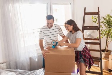 Güzel genç bir kadın ambalaj makinesi kullanıyor, karton kutuları kaydediyor, taşınmaya hazırlanıyor, taşınırken eşyalar paketleniyor.