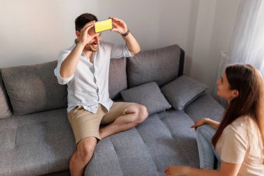 Çift evde birlikte vakit geçirirken sessiz sinema oynayarak eğleniyor, akıllı bir telefon uygulamasından kelimeleri izah ediyor ve tahmin ediyor.