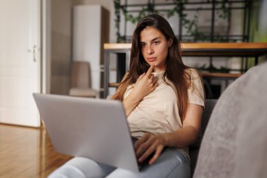 Kucağında dizüstü bilgisayarla kanepede uzanan güzel genç bir kadın online kursa gidiyor, internetten öğreniyor.