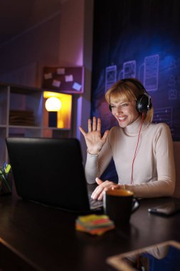 Ofisteki masasında oturan bir kadın, evden uzaktan çalışıyor, kulaklık takıyor ve internet üzerinden toplantı yapıyor.