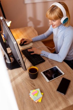 Ofisindeki masasında oturan kadın yazılım geliştirici masaüstü bilgisayarında kulaklık kodlaması takıyor
