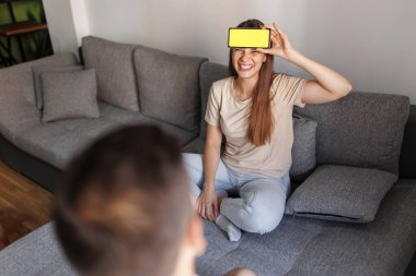 Çift evde sessiz sinema oynayarak eğleniyor, akıllı telefon uygulamasından gelen kelimeleri açıklıyor ve tahmin ediyor.