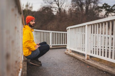 Aktif genç adam köprü çitlerine yaslanıyor ve koşuya ara veriyor, sabah antrenmanı yapıyor.