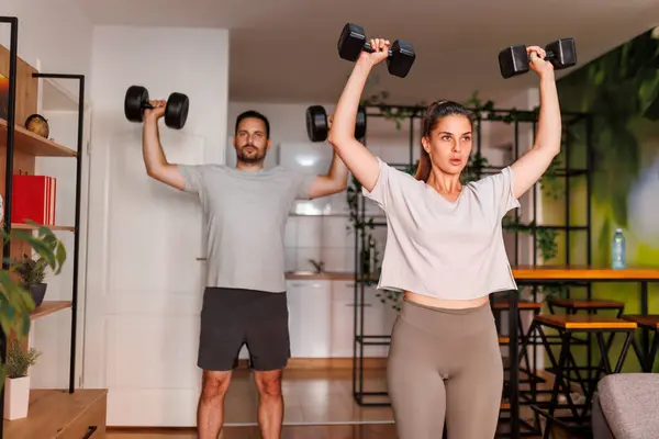 活跃的年轻夫妇在家里一起锻炼时 用哑铃做二头肌运动 — 图库照片