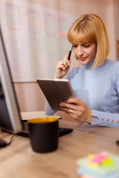 自宅のオフィスで机に座り タブレットコンピュータを使ってオンラインコースを受講し 勉強しながらプランナーで執筆する女性 — ストック写真