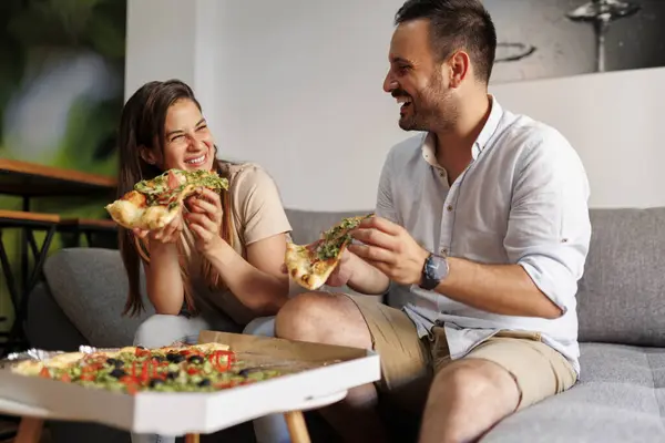 Beautiful young couple in love relaxing at home, eating pizza and having fun spending time together
