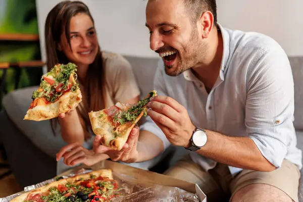 Beautiful young couple in love relaxing at home, eating pizza and having fun spending time together