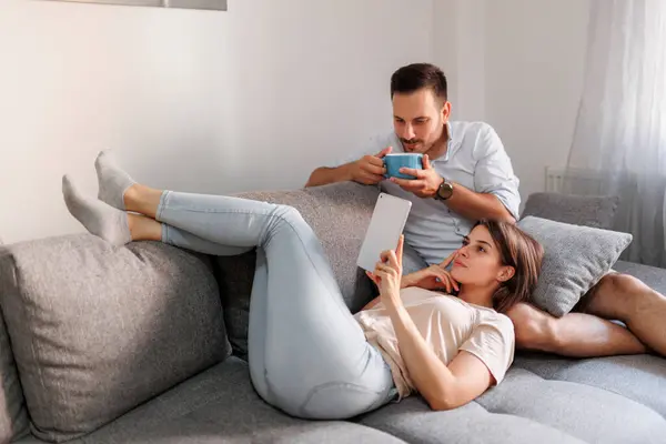 美しい若いカップルは 自宅でリラックスして タブレットコンピュータを使用してインターネットをサーフィンし 朝にコーヒーを飲む — ストック写真