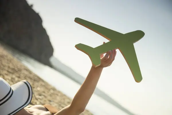 Female hand holding a cardboard airplane with the seascape in the background. Summer vacations transportation advertisement