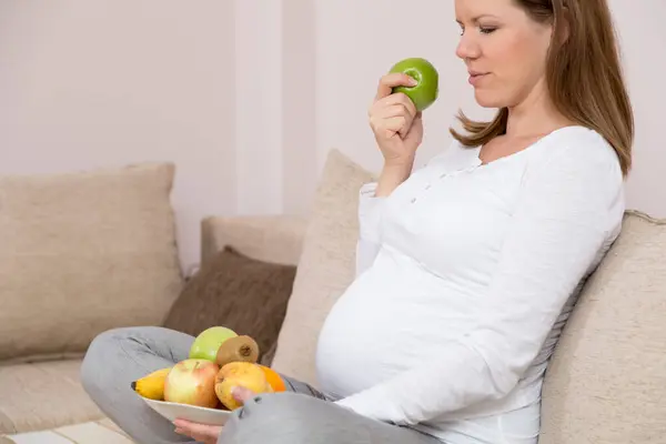 Pregnant Woman Sitting Couch Holding Bowl Fruit Eating Apple — Stock Photo, Image