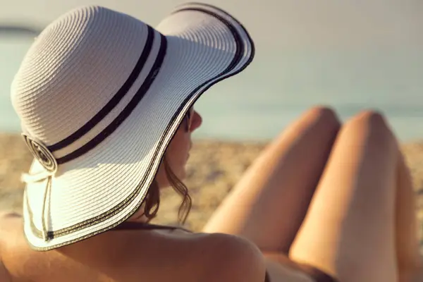 Woman wearing bikini and a straw hat lying on the sand on the beach and sunbathing. Summer vacations travel relaxation time. Focus on the hat