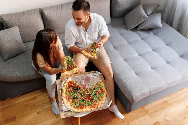 High angle view of beautiful young couple in love relaxing at home, eating pizza and having fun spending time together