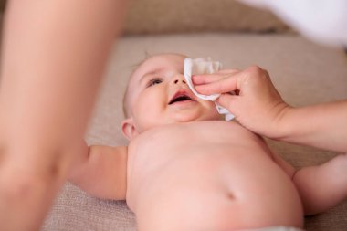 Anne yüzünü silerken ve banyo yaptıktan sonra üzerini değiştirirken küçük tatlı çocuğun gülümsemesini yüksek açılı görüyor. Ağzına odaklan ve elini sil.