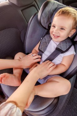 Annesinin küçük bebeğini bebek koltuğuna bağlayıp çocuğuyla güvenli bir sürüş için hazırlandığı yüksek açılı manzara.