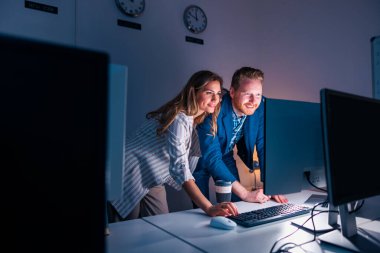 İş arkadaşları ofiste fazla mesai yapıyor, belgeleri inceliyor ve yeni bir proje üzerinde çalışıyorlar.