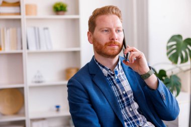 Modern genç işadamı ofiste çalışırken telefonla konuşuyor, ciddi ve düşünceli.