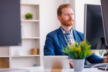Ofiste çalışırken masaüstü bilgisayarını kullanan başarılı bir iş adamı.