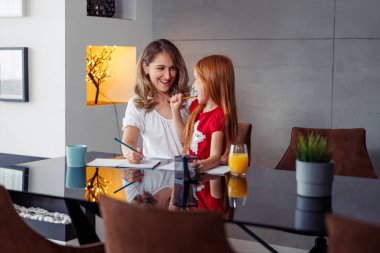 Anne kızını kucağında tutuyor, ona evde ders veriyor ve ev ödevlerine yardım ediyor, mektup ve yazma alıştırması yapıyor; evde eğitim ve uzak öğrenim kavramı