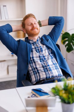 Kendine güvenen başarılı bir işadamı ofisinde çalışırken dinleniyor, gülümsüyor ve esniyor.