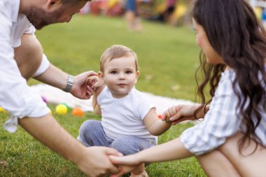 Anne ve baba parkta erkek çocuklarıyla oynarken, el ele tutuşurken, daireler çizerken ve çocuk şarkıları söylerken eğleniyorlar.