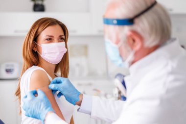 Aşı yaptıktan sonra hastaya tıbbi yama uygulayan doktor; hastanede kovid 19 veya mevsimsel grip aşısı alan genç kadın - aşı, aşı ve hastalık önleme kavramı