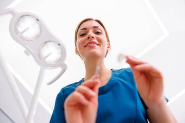 Kadın dişçinin, hastaların dişlerini kontrol ederken açı aynasını tutuşu düşük açılı.