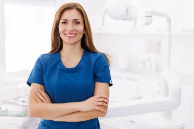 Acil serviste kollarını kavuşturup gülümseyen, üniformalı başarılı, kendine güvenen genç bir kadın doktorun portresi.