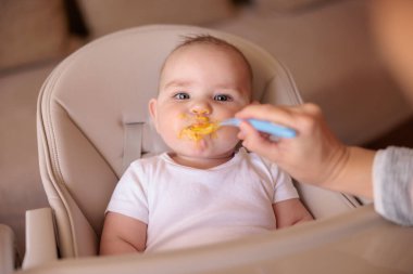 Sevimli erkek bebek yüksek sandalyede oturuyor. Dağınık ve kararlı. Yulaf lapası yemeyi reddediyor. 