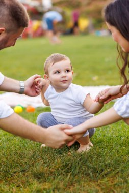 Anne ve baba parkta erkek çocuklarıyla oynarken, el ele tutuşurken, daireler çizerken ve çocuk şarkıları söylerken eğleniyorlar.