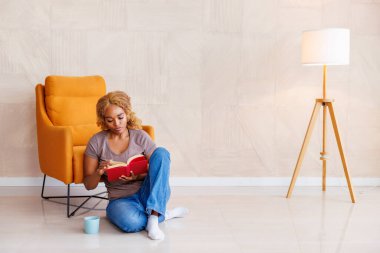 Güzel bir kadın evde dinleniyor, kahve içiyor ve kitap okuyor.