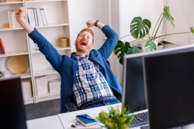 Kendine güvenen başarılı bir işadamı ofisinde çalışırken dinleniyor, gülümsüyor ve esniyor.