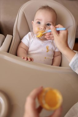 Annesinin küçük tatlı çocuğu lapayla beslediği yüksek açılı bir manzara. Bebek sandalyede oturuyor, gülümsüyor ve yemek yiyor.
