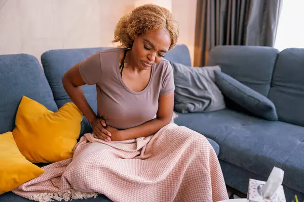 Frau Sitzt Auf Wohnzimmercouch Mit Decke Bedeckt Hat Bauchschmerzen Als — Stockfoto