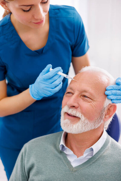 Врач применяет кожные наполнители к пациенту старшего возраста; пожилой человек получает антивозрастное лечение гиалуроновой кислотой