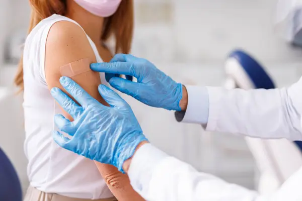 Close up of doctor applying medical patch to patient after injecting vaccine; young woman receiving covid 19 or seasonal flu vaccine in hospital - vaccination, immunization and disease prevention concept