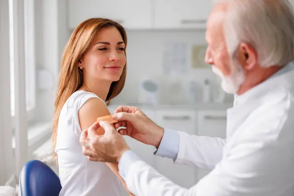 General practitioner applying medical patch to patient after injecting vaccine; young woman receiving seasonal flu vaccine in hospital - vaccination, immunization and disease prevention concept
