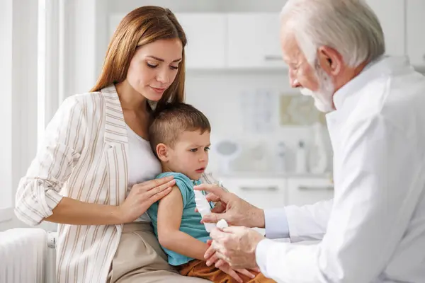 Mor Som Håller Sin Son Knät Medan Han Vaccineras Läkare Royaltyfria Stockbilder