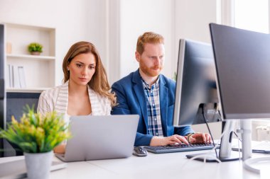 Ofiste birlikte çalışırken dizüstü bilgisayar ve masaüstü bilgisayar kullanan başarılı, kendine güvenen iş adamları; yazılım geliştiricileri kodlama