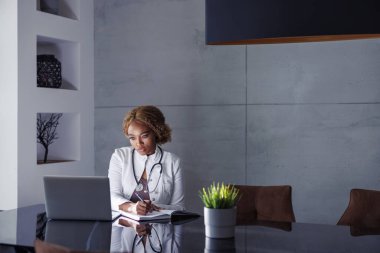 İnternette seminer veren kadın doktor, online kurs alırken not yazan, hastalarla görüntülü konuşma yapan ev ofisinden uzaktan çalışan.