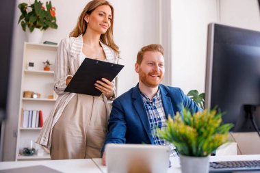 İş arkadaşları bir ofiste birlikte çalışıyor, sabah brifingi veriyor, evrak işlerini yapıyor ve belgeleri inceliyor.
