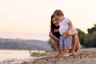 Güzel, genç bir anne, yaz öğleden sonrasını sahilde birlikte geçirirken oğluyla eğleniyor. Ona sarılıyor ve suya çakıl taşları atıyor.