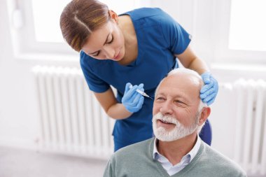 Doktor üst düzey erkek hastaya deri dolguları uyguluyor; kıdemli adam hyaluronik asit anti-yaş tedavisi görüyor