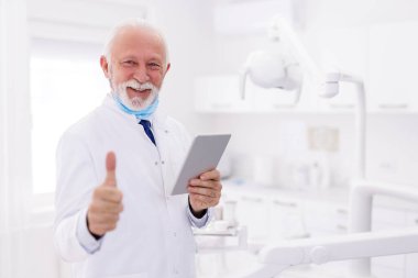 Tablet bilgisayar kullanarak tıbbi kayıtları incelerken hastanede dikilen üniformalı kıdemli erkek doktorun portresi.